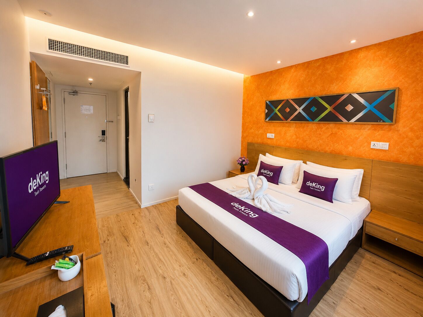 A hotel room with a bed, a TV, a desk, and a painting on the wall.