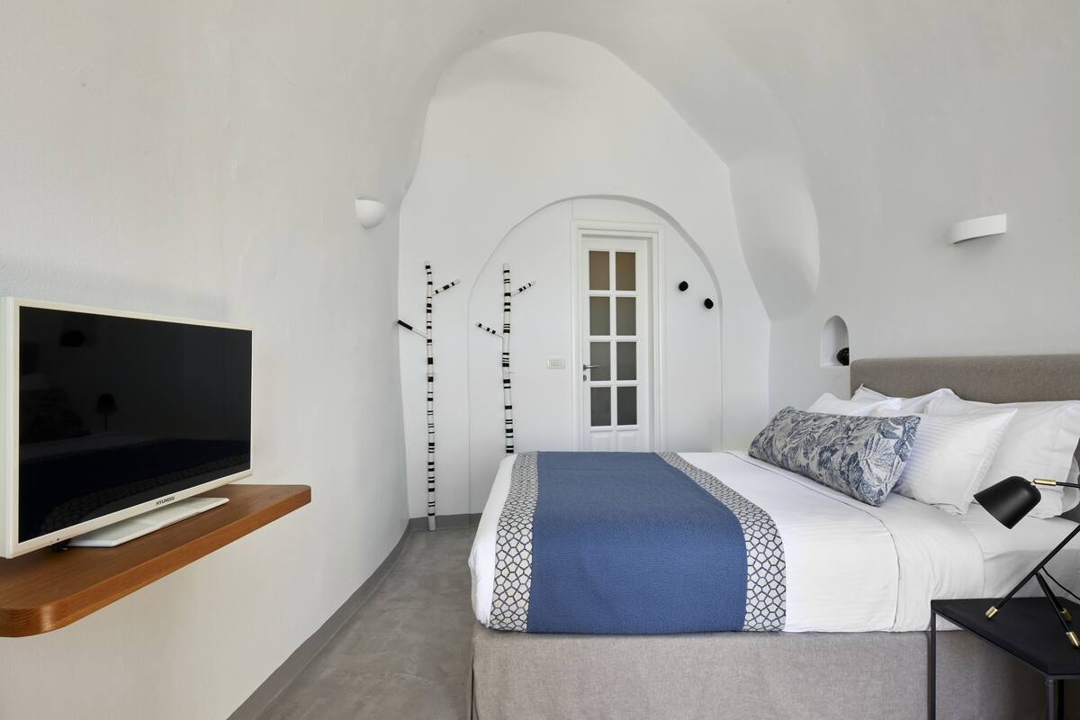 Un dormitorio moderno con una cama, un televisor en un estante, una puerta y una lámpara fijada a la pared.