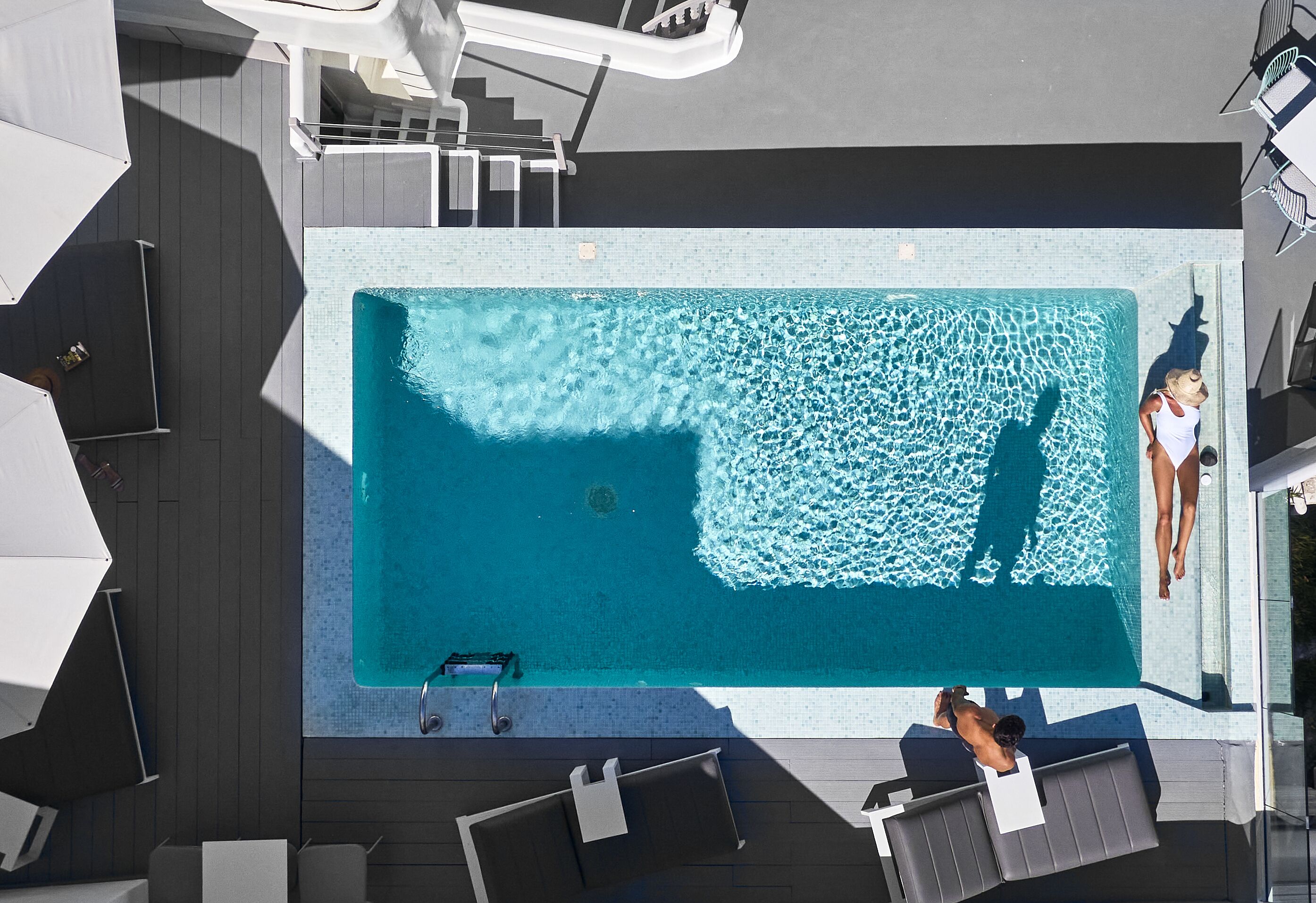 An aerial view of a swimming pool with lounge chairs and a person diving into the water.
