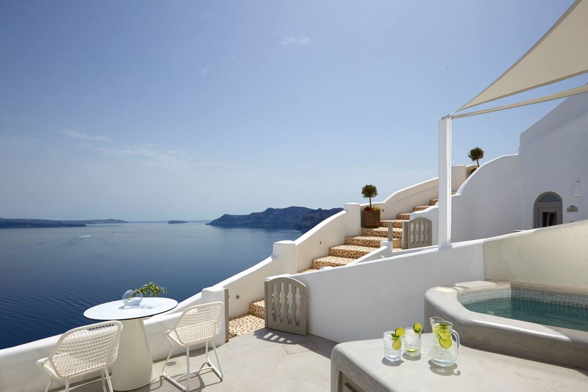 Una terraza con piscina, mobiliario blanco y vista al mar.
