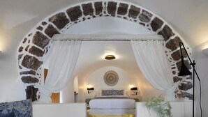 Un dormitorio con un arco de piedra, una cama con ropa blanca, un adorno en la pared y una lámpara de noche.