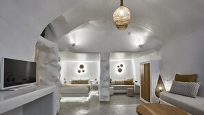 Un interior moderno con una paleta de colores blancos, un televisor sobre un mueble bajo, un sofá, una mesa de centro y una lámpara colgante.