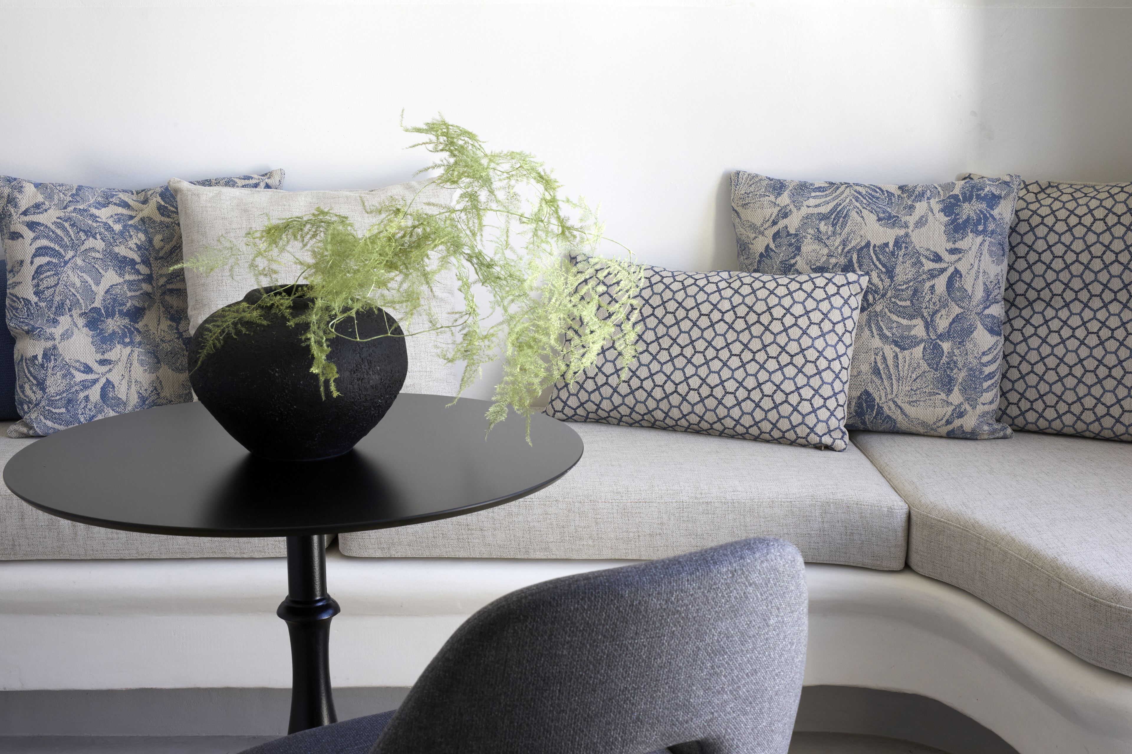 A modern living room with a round black table, a grey sofa, and patterned cushions.