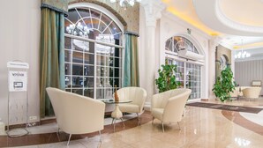Eine Lobby mit einer Kronleuchter, einer Rezeption und einer Sitzecke mit Stühlen und einem kleinen Tisch.