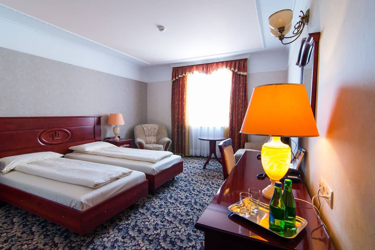 A hotel room with two beds, a desk with a lamp, a chair, a small table, and a window with curtains.