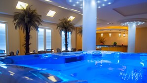 Ein großes, beheiztes Whirlpool-Becken im Innenbereich mit blauem Licht, umgeben von Palmen und einem modernen Design.