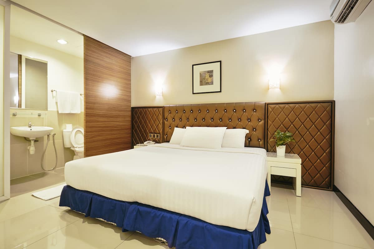Een moderne hotelkamer met een groot bed, een nachtkastje met een plant erop, een wandlamp en een zichtbare badkamer door een geopende deur.