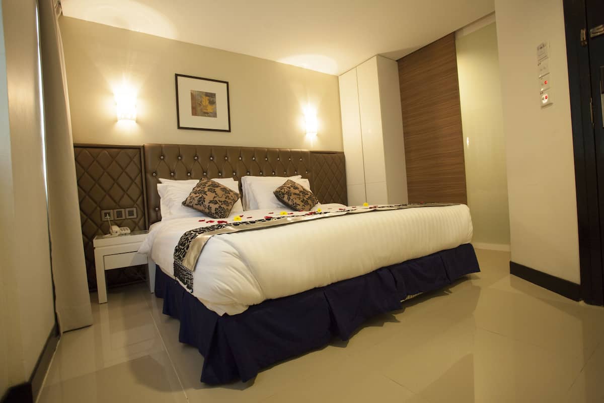 Een netjes opgemaakt bed met een decoratief hoofdbord, een nachtkastje met een lamp en een wandlamp.