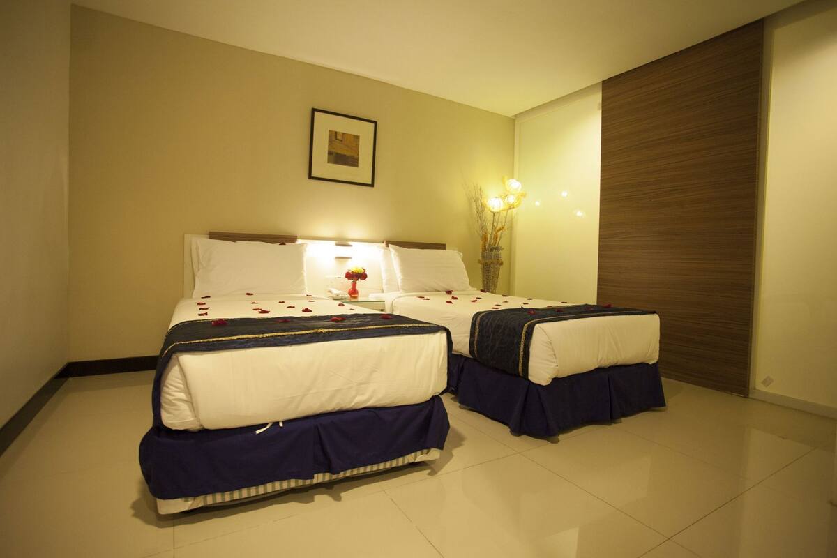 Een hotelkamer met twee bedden, een nachtkastje met een bloevas en een lijst aan de muur.
