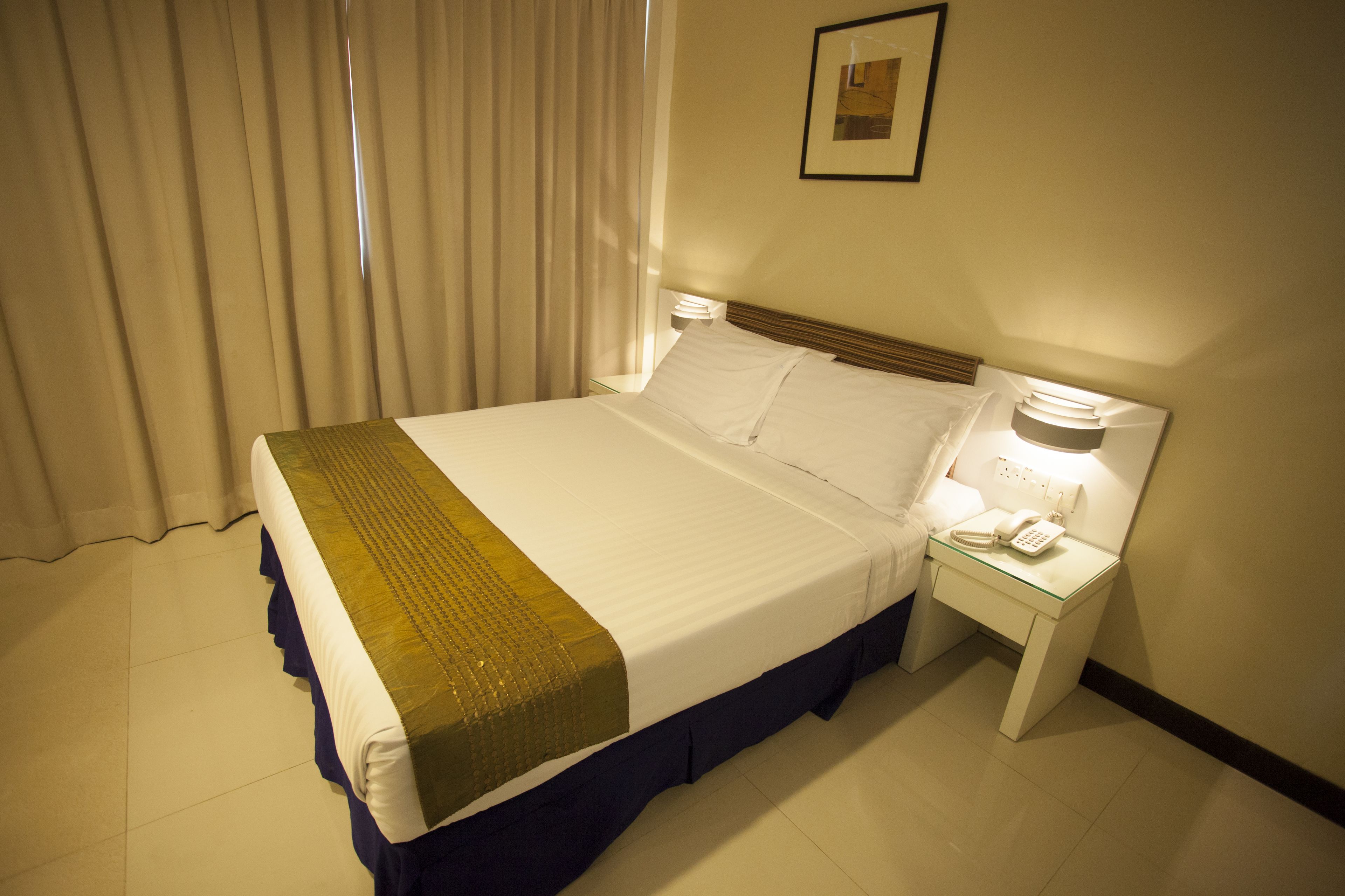 Een hotelkamer met een bed, nachtkastje met een lamp en een telefoon.