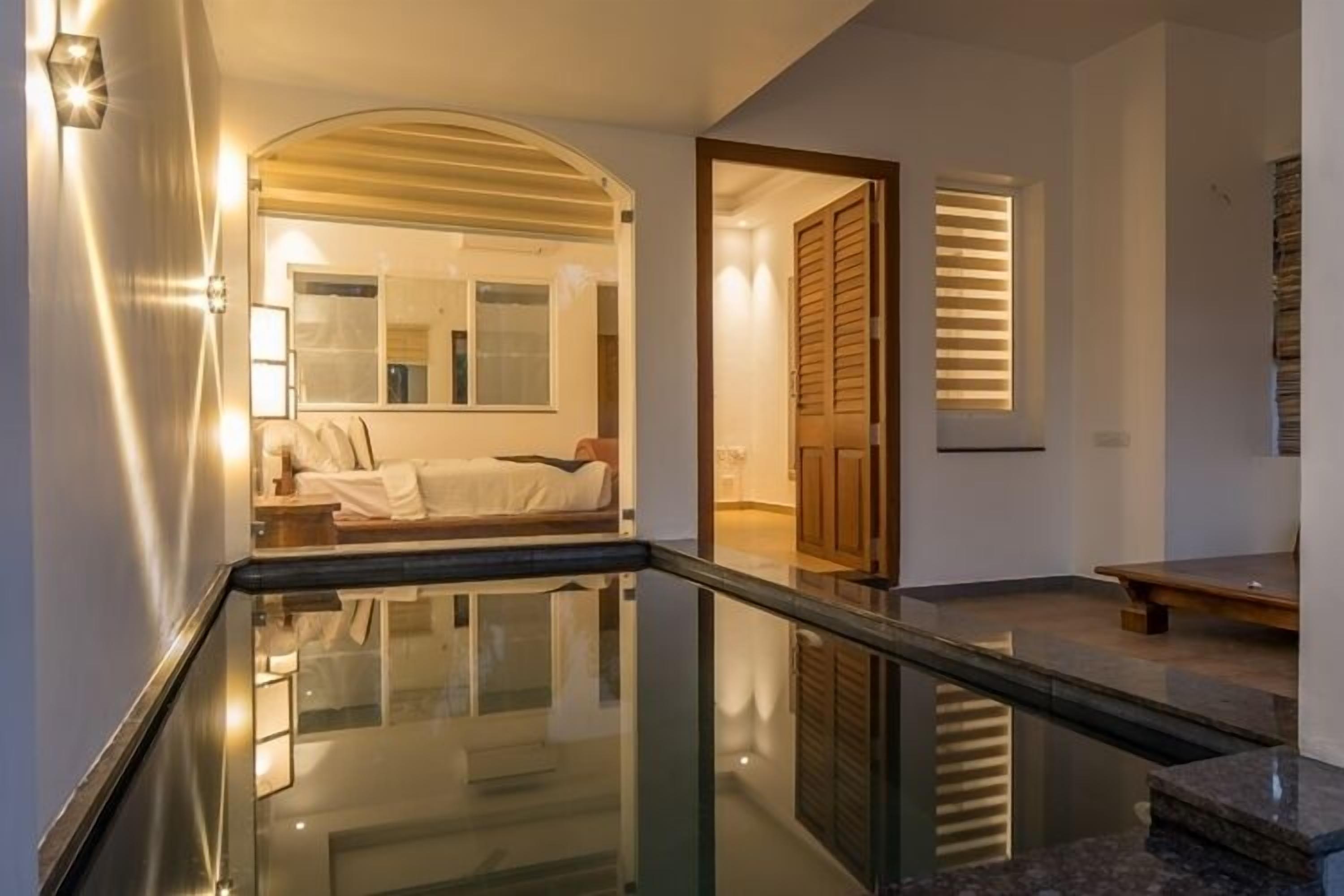 A modern hotel room with a glass-enclosed pool, a large mirror, and a cozy seating area.