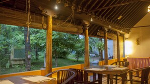 A restaurant with wooden furniture and a view of a lush garden. - Over The Hill (Neyyattinkara)