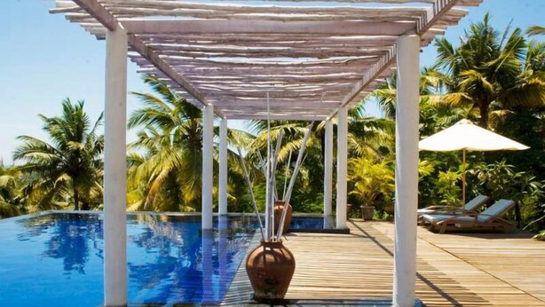 A pool area with a pergola, palm trees, and lounge chairs. - Over The Hill (Neyyattinkara)