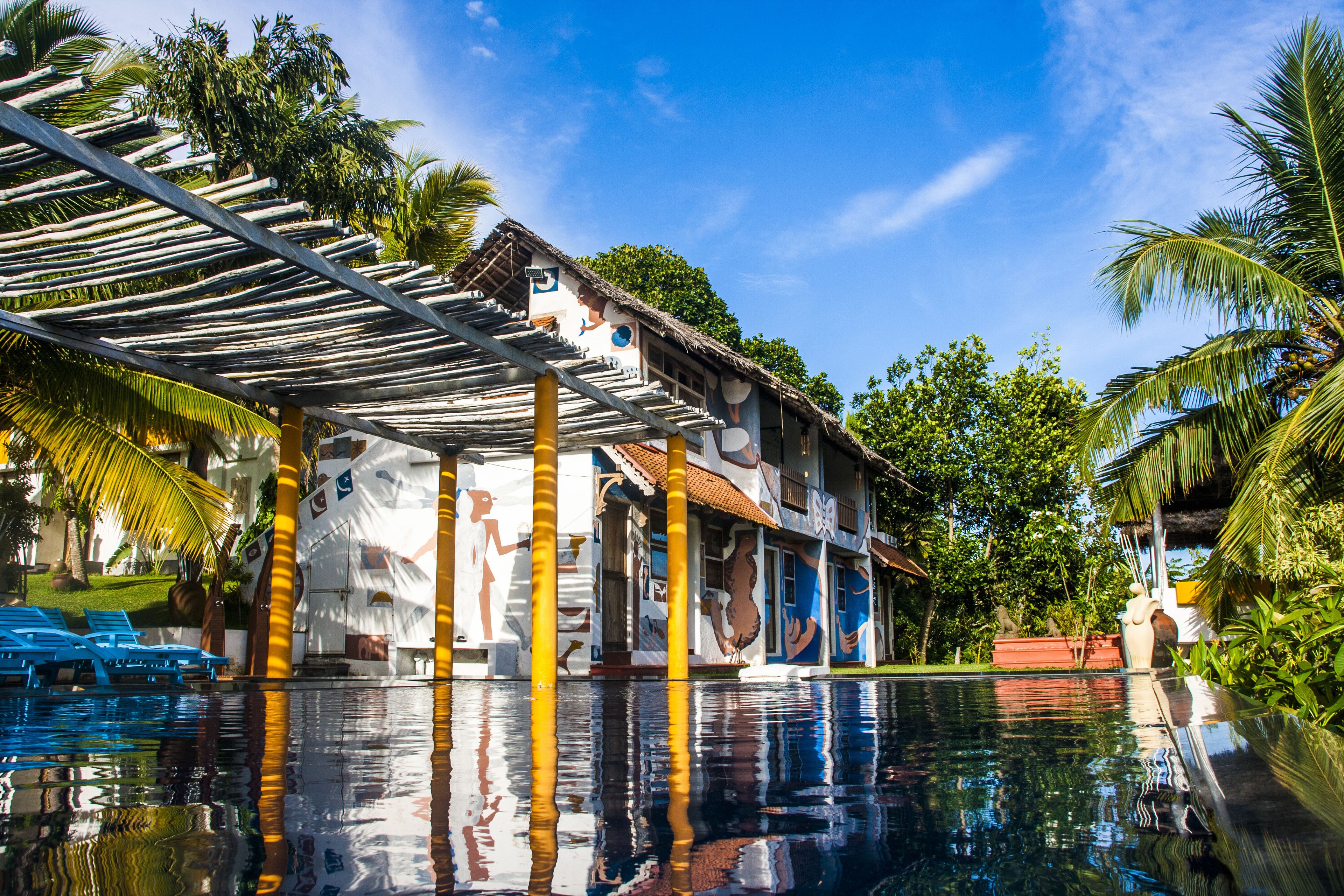 Un área junto a la piscina con vista despejada, un espacio de estar techado y un edificio con murales coloridos.