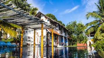 Un área junto a la piscina con vista despejada, un espacio de estar techado y un edificio con murales coloridos.