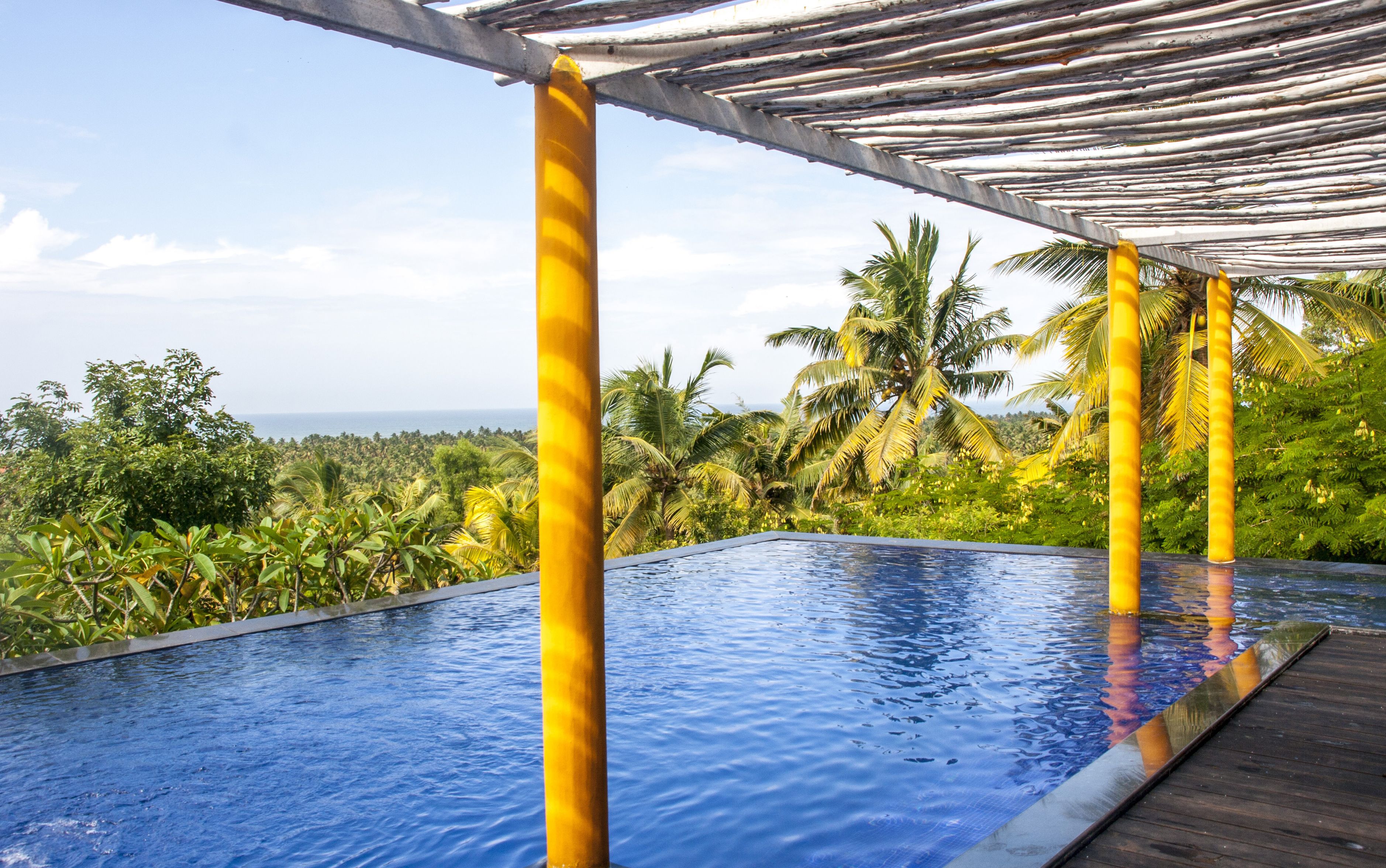 A pool with a wooden deck and a metal pergola.