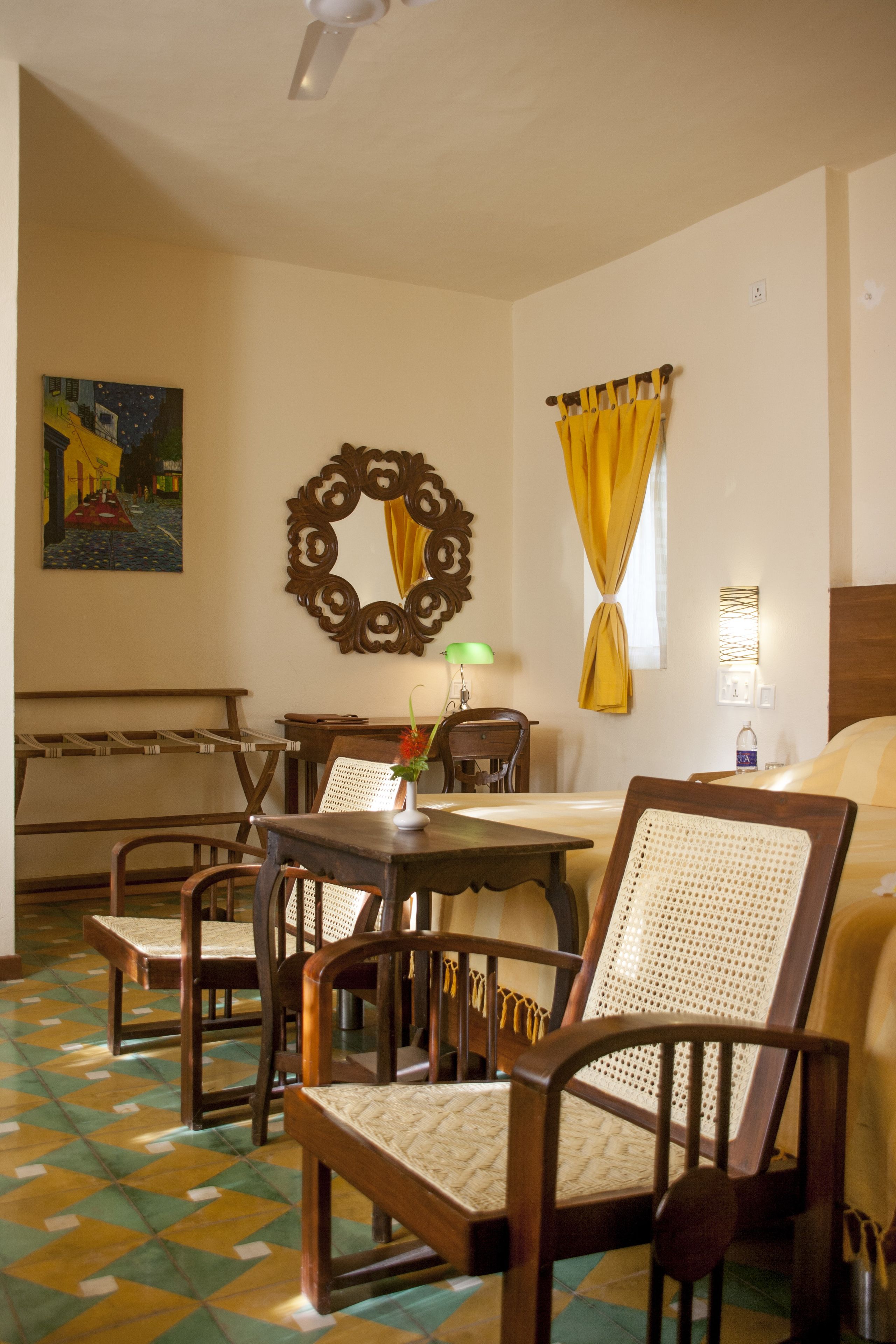 A hotel room with a dining table, chairs, a bed, a mirror, and a painting on the wall.