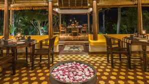 An outdoor dining area with hexagonal patterned flooring, wooden tables and chairs, and a central flower arrangement. - Over The Hill (Neyyattinkara)