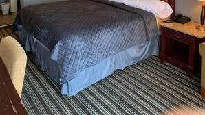 Habitació d'hotel amb un llit gran, dues taules de nit, un rellotge de paret i una obra d'art emmarcada.