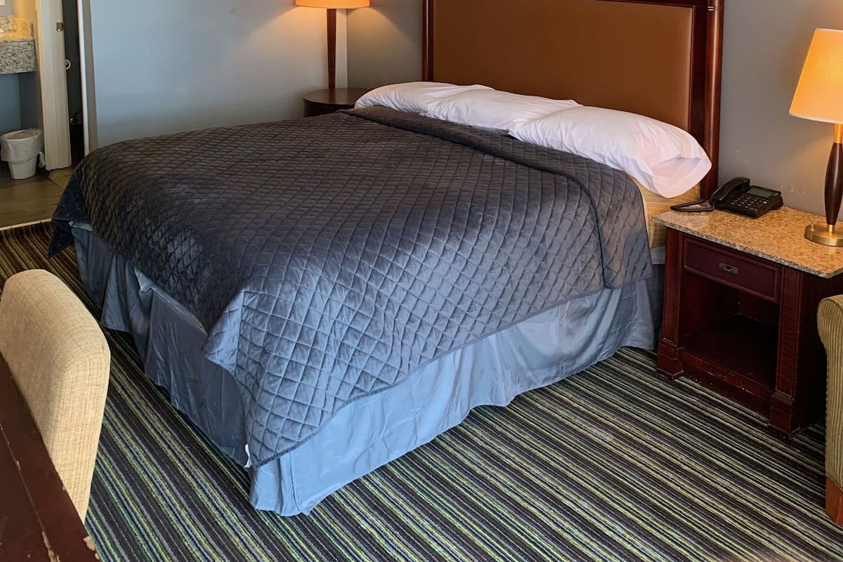 A hotel room with a large bed, two bedside tables, a wall clock, and a framed artwork.