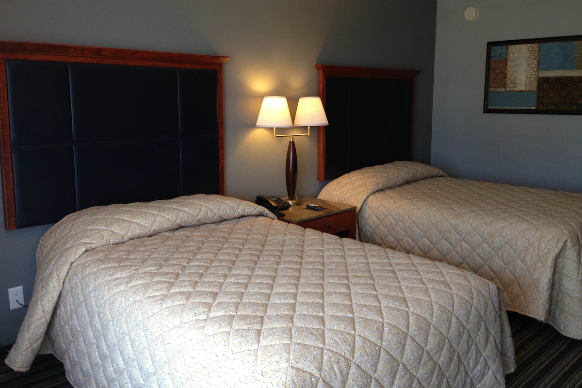 A hotel room with two beds, a nightstand with a lamp, and a painting on the wall.