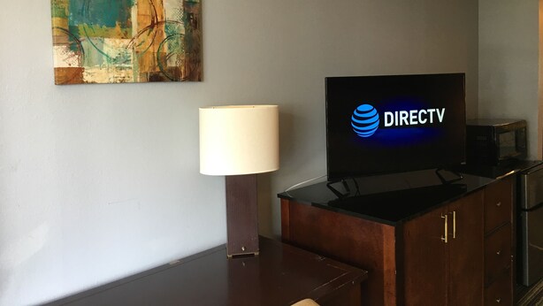 Habitació d'hotel amb el logotip de DIRECTV a la televisió, una làmpada i una obra d'art abstracta a la paret.