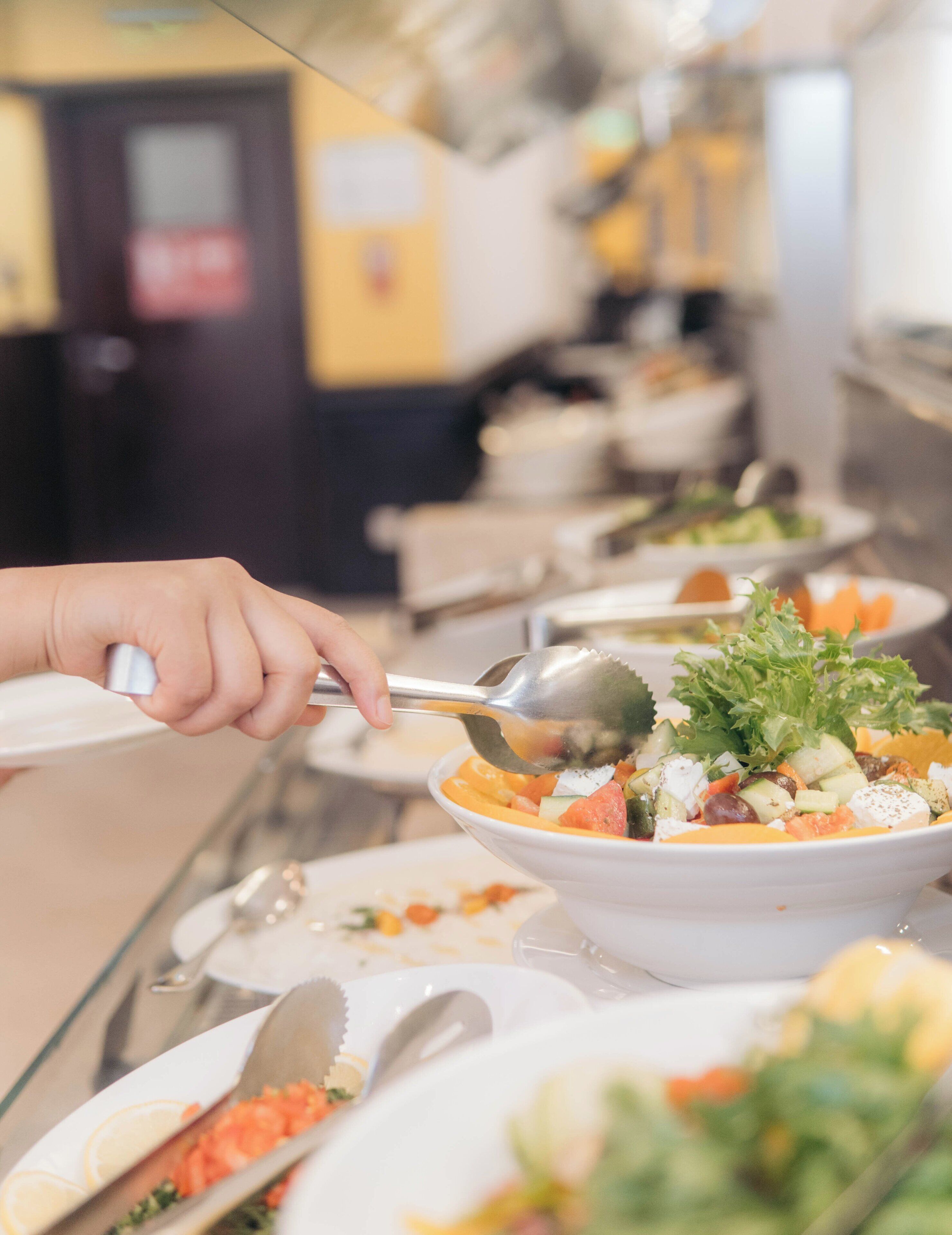A buffet setup with various dishes, including a salad with lettuce and cheese, and a person using a spoon to serve themselves.