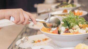 A buffet setup with various dishes, including a salad with lettuce and cheese, and a person using a spoon to serve themselves.