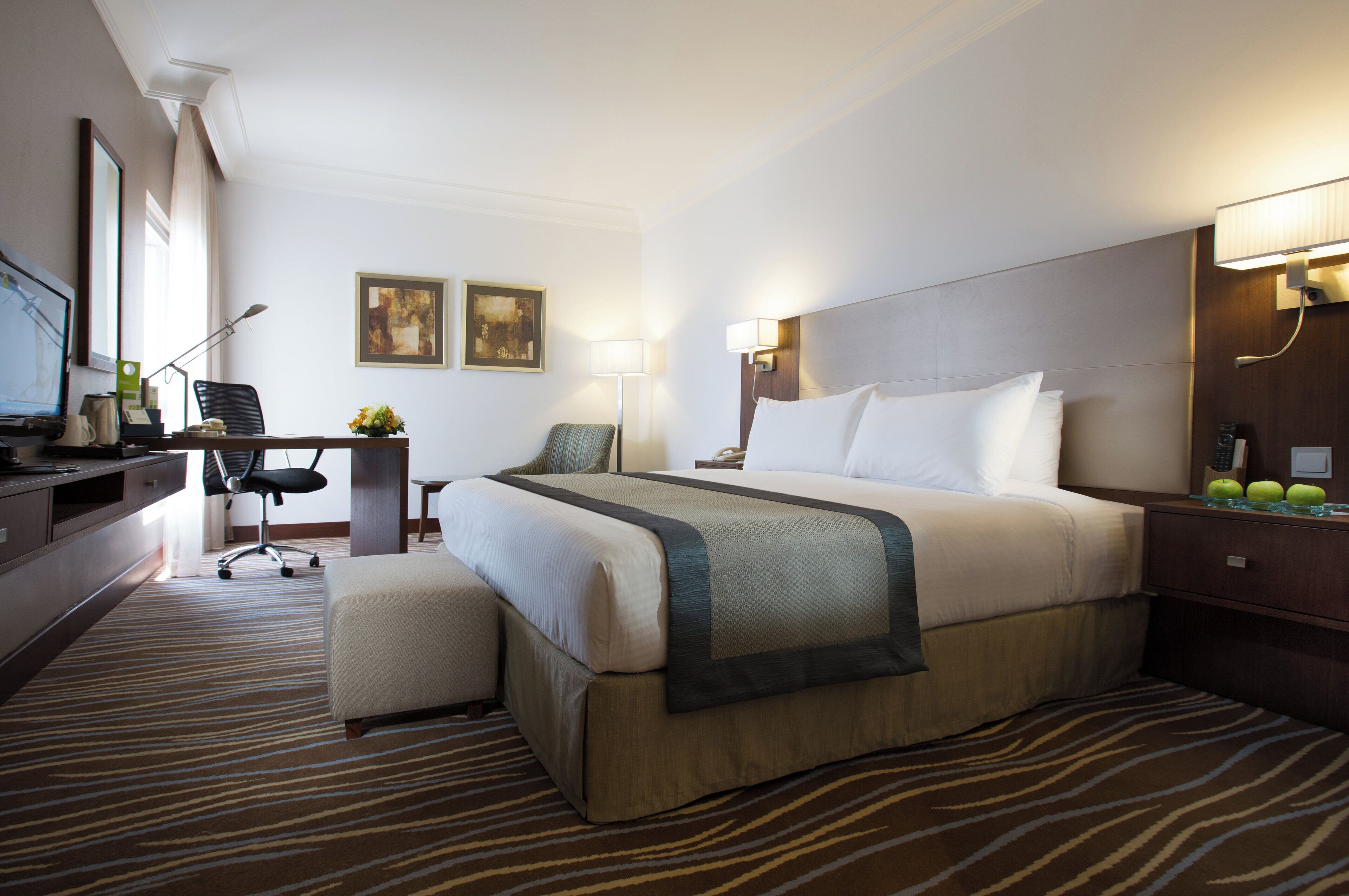 Una habitación de hotel con una cama grande, un escritorio con silla, un televisor y una lámpara.