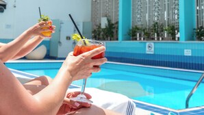 A person relaxing by a poolside with a drink in hand, a pool, and a building with a blue facade in the background. - Copthorne Downtown Abu Dhabi (Abu Dhabi)