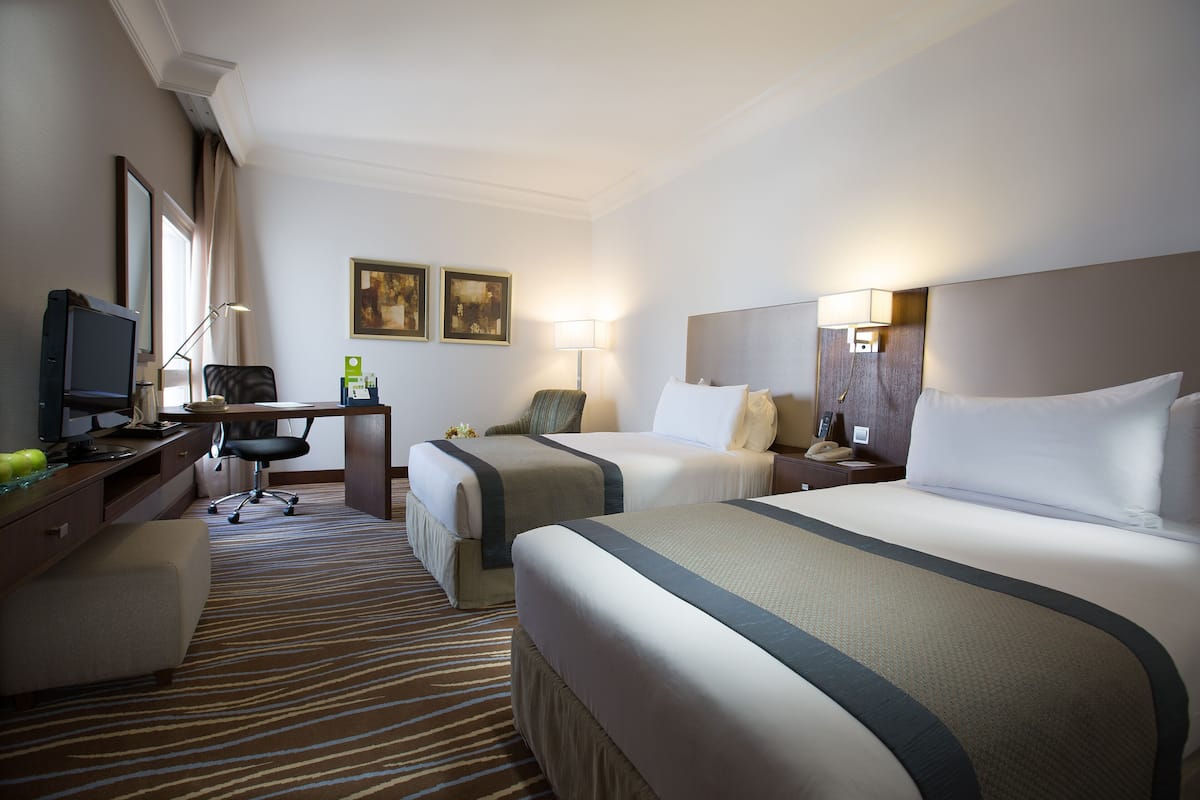 Habitación de hotel con dos camas, un escritorio, una silla, un televisor y una lámpara.