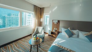 A hotel room with a large bed, a small table with fruit, a chair, a nightstand, and a view of the city through large windows. - Copthorne Downtown Abu Dhabi (Abu Dhabi)