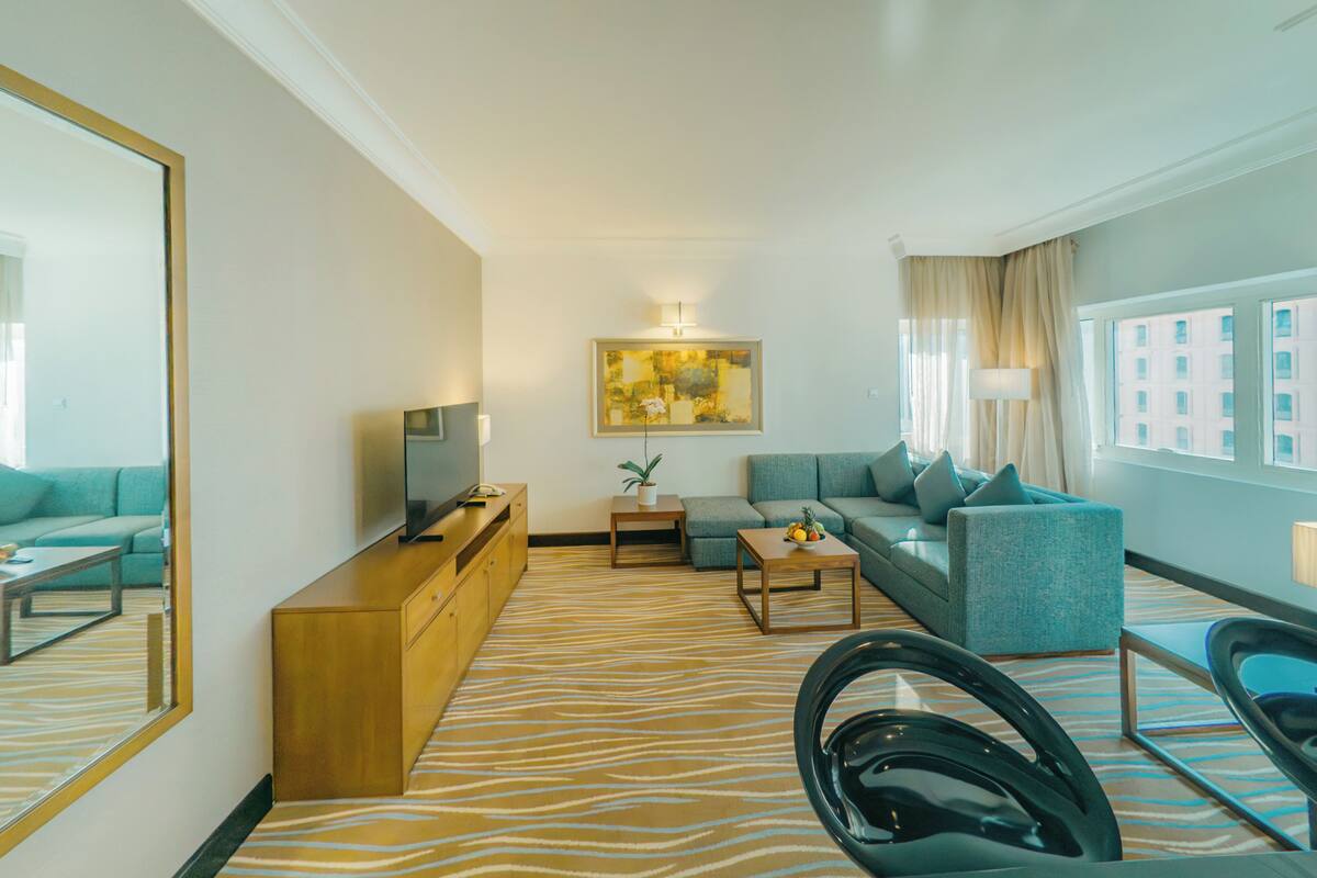 Una habitación de hotel moderna con alfombra estampada de cebra, un sofá, una mesita, un televisor y un espejo.