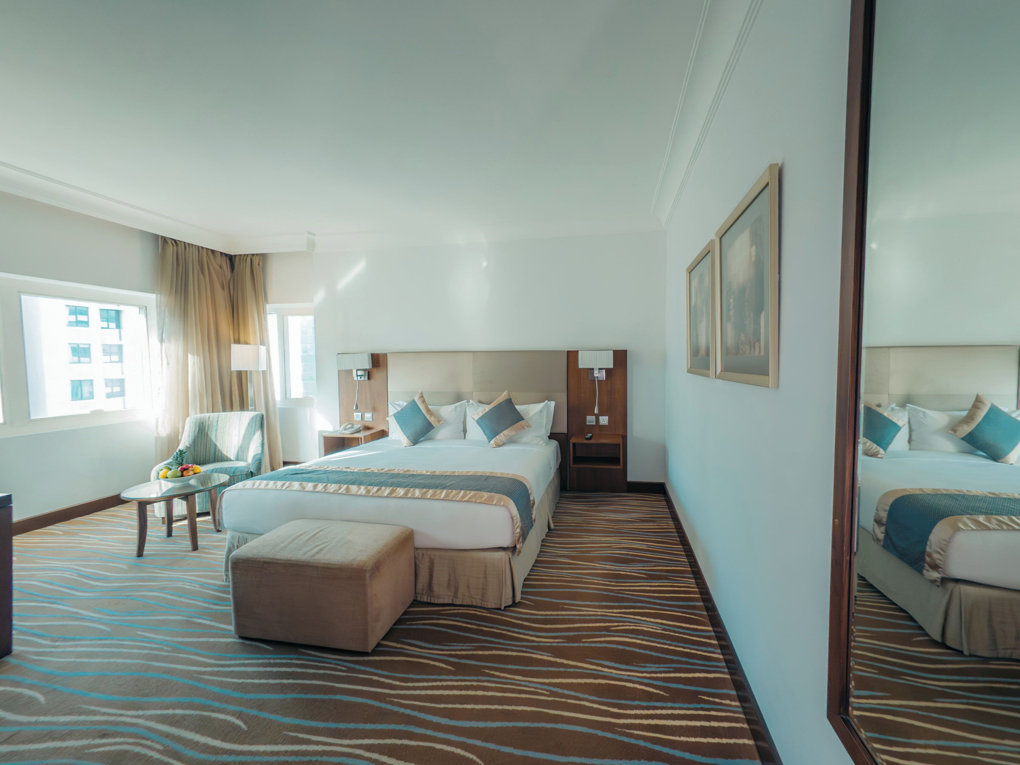 A hotel room with a large bed, a chair, a small table with fruit, and a mirror.