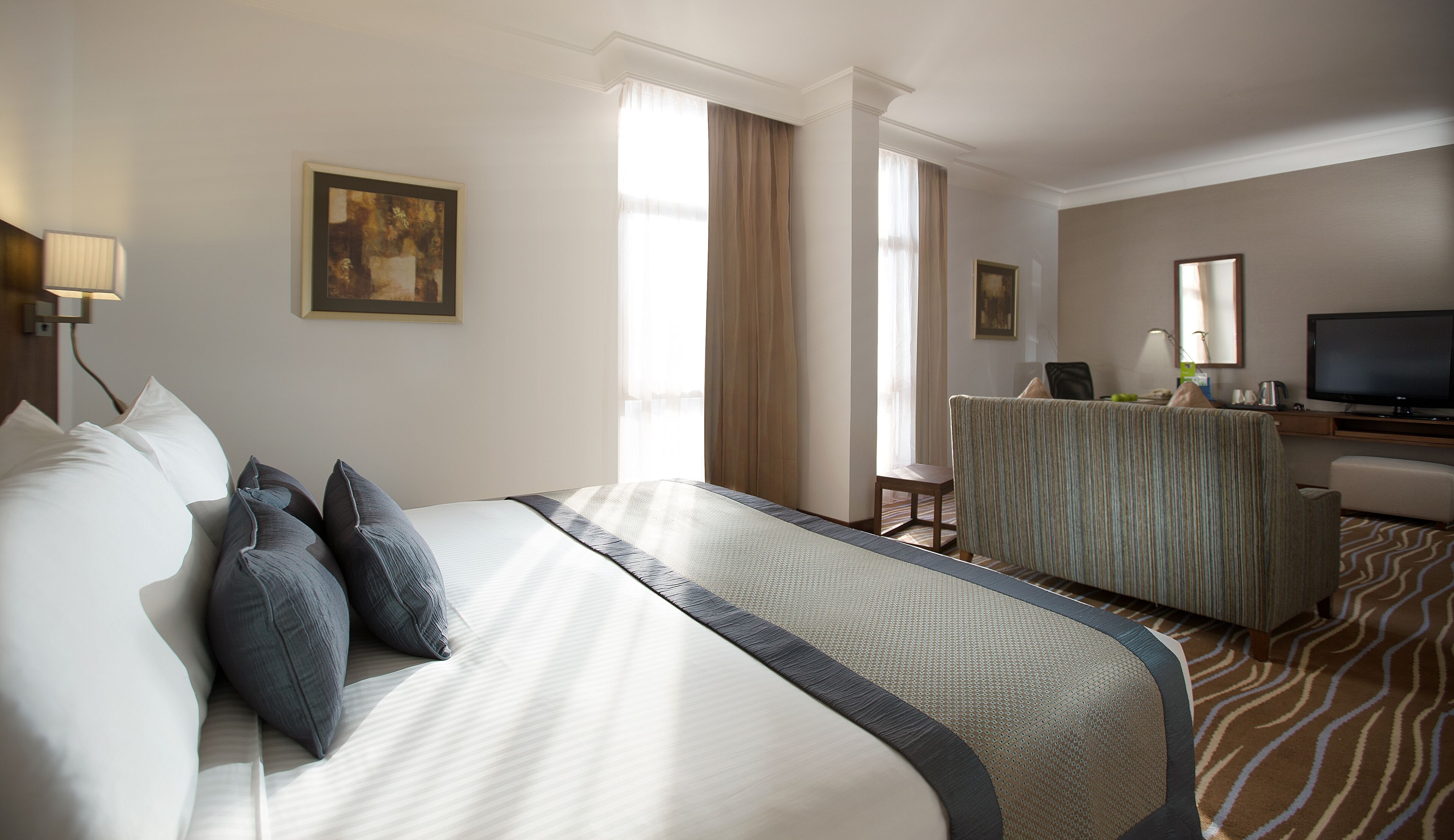 A hotel room with a large bed, a desk, a television, and a window with curtains.