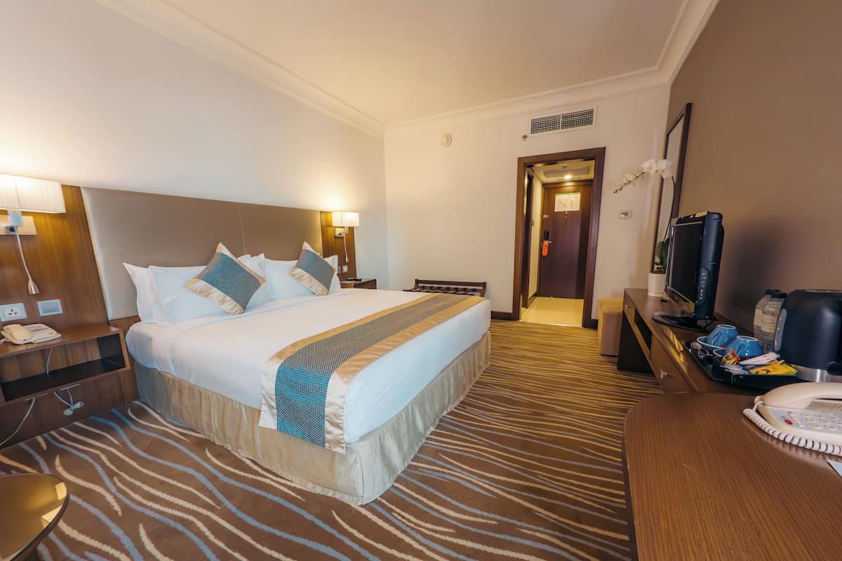 Una habitación de hotel con una cama grande, mesitas de noche, un escritorio con computadora y televisión.