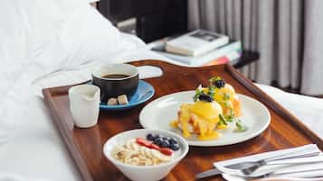 Un plateau de petit-déjeuner avec des œufs Bénédicte, du café et des fruits rouges frais, posé sur un lit d’hôtel.