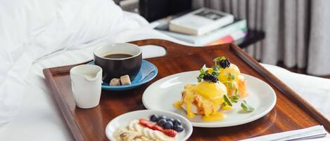 Bandeja de desayuno con huevos Benedict, café y bayas frescas sobre una cama de hotel.