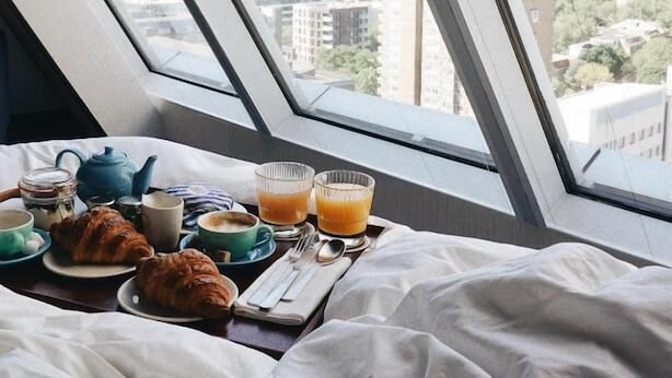 A bed with a city view, breakfast items, and a window with a cityscape. - Montcalm East, Autograph Collection (London)