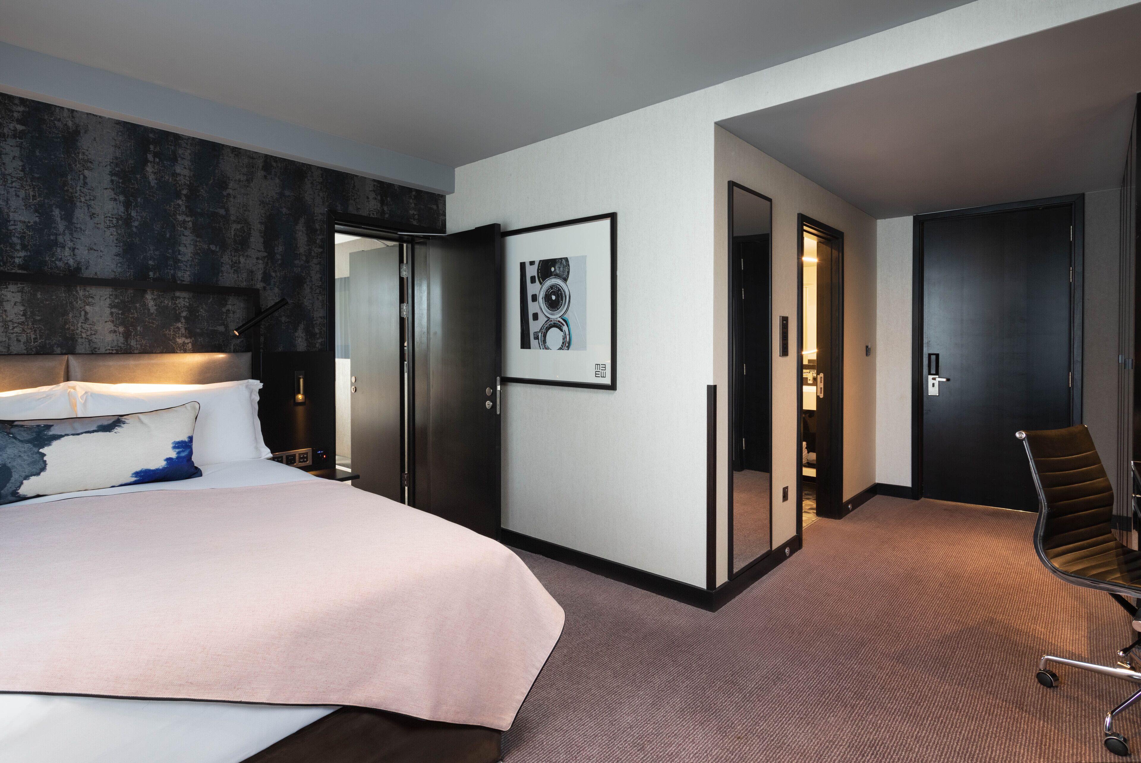 A hotel room with a large bed, a desk, a chair, and a framed picture on the wall.