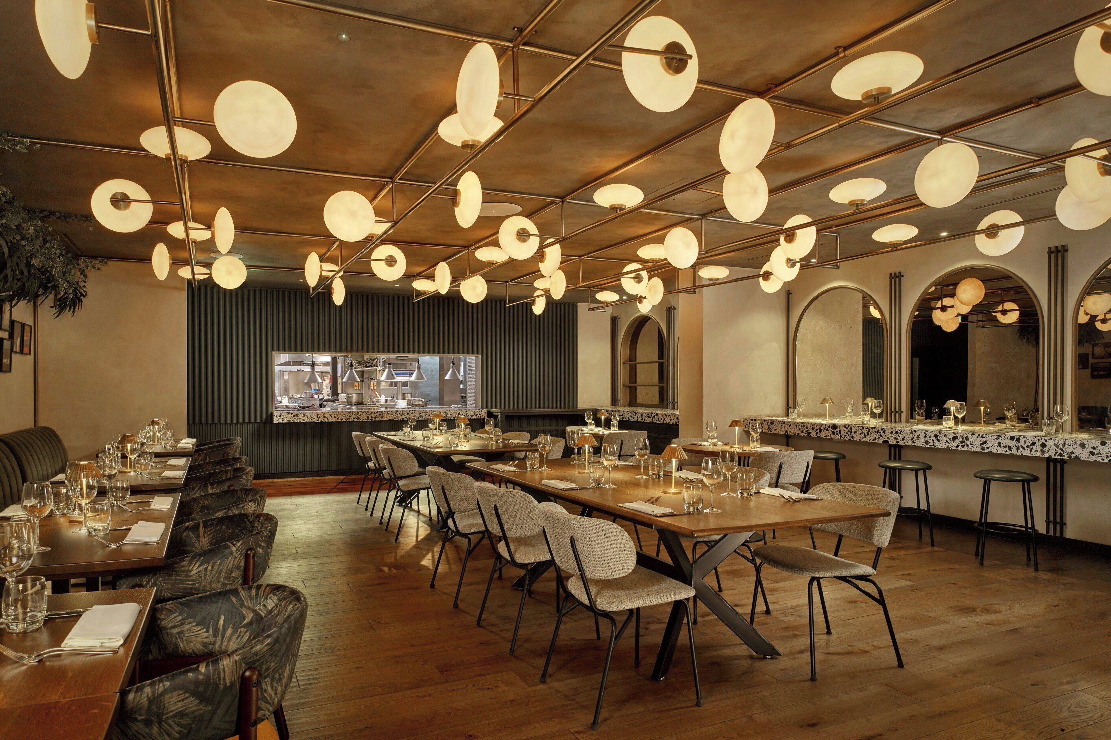 A restaurant with a long dining table, multiple chairs, and hanging spherical light fixtures.