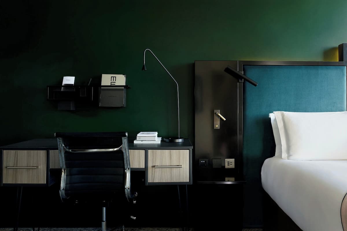 A hotel room with a desk, chair, and a bed.