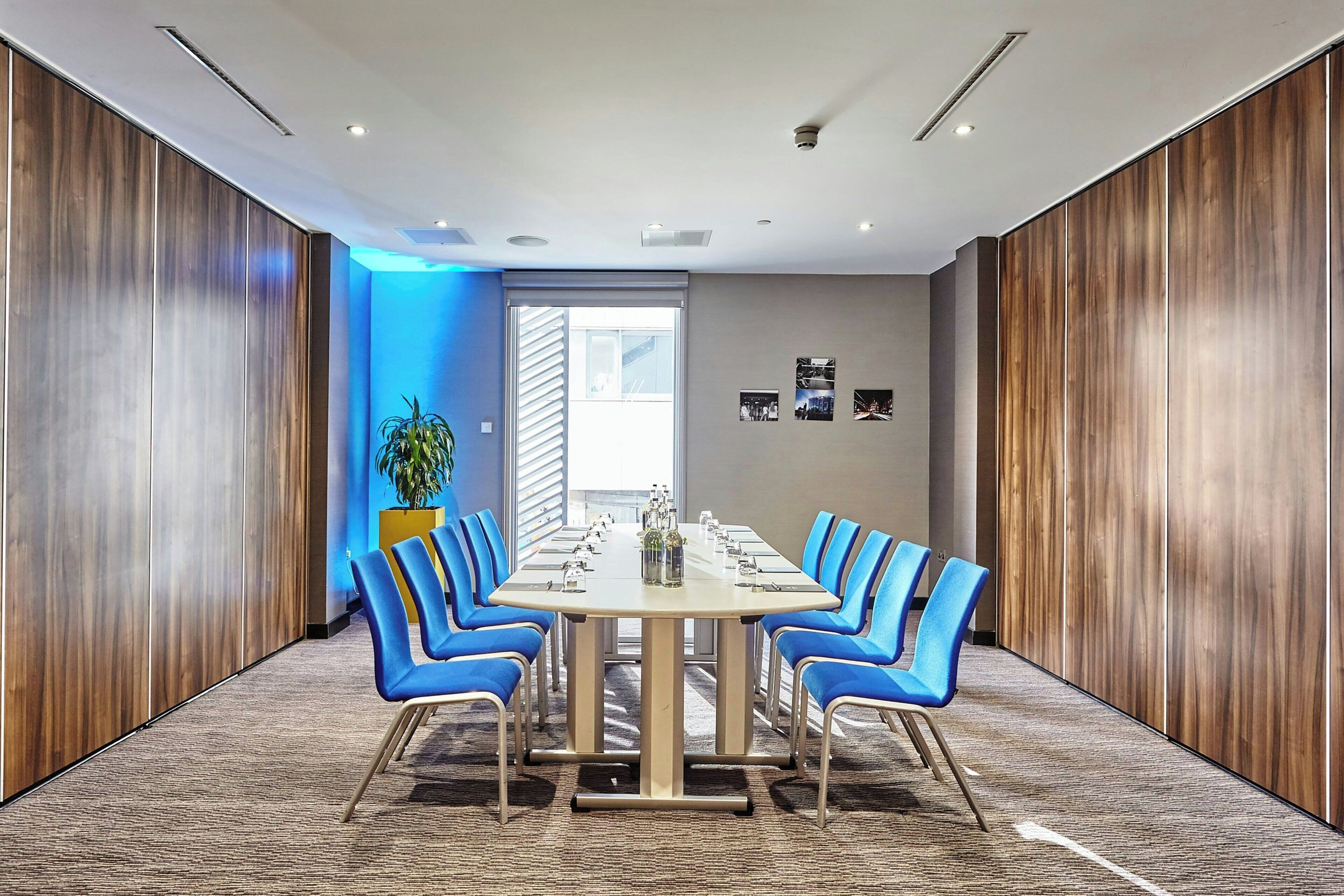 A conference room with a long table, blue chairs, and wooden panel walls.
