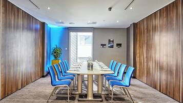 A conference room with a long table, blue chairs, and wooden panel walls.