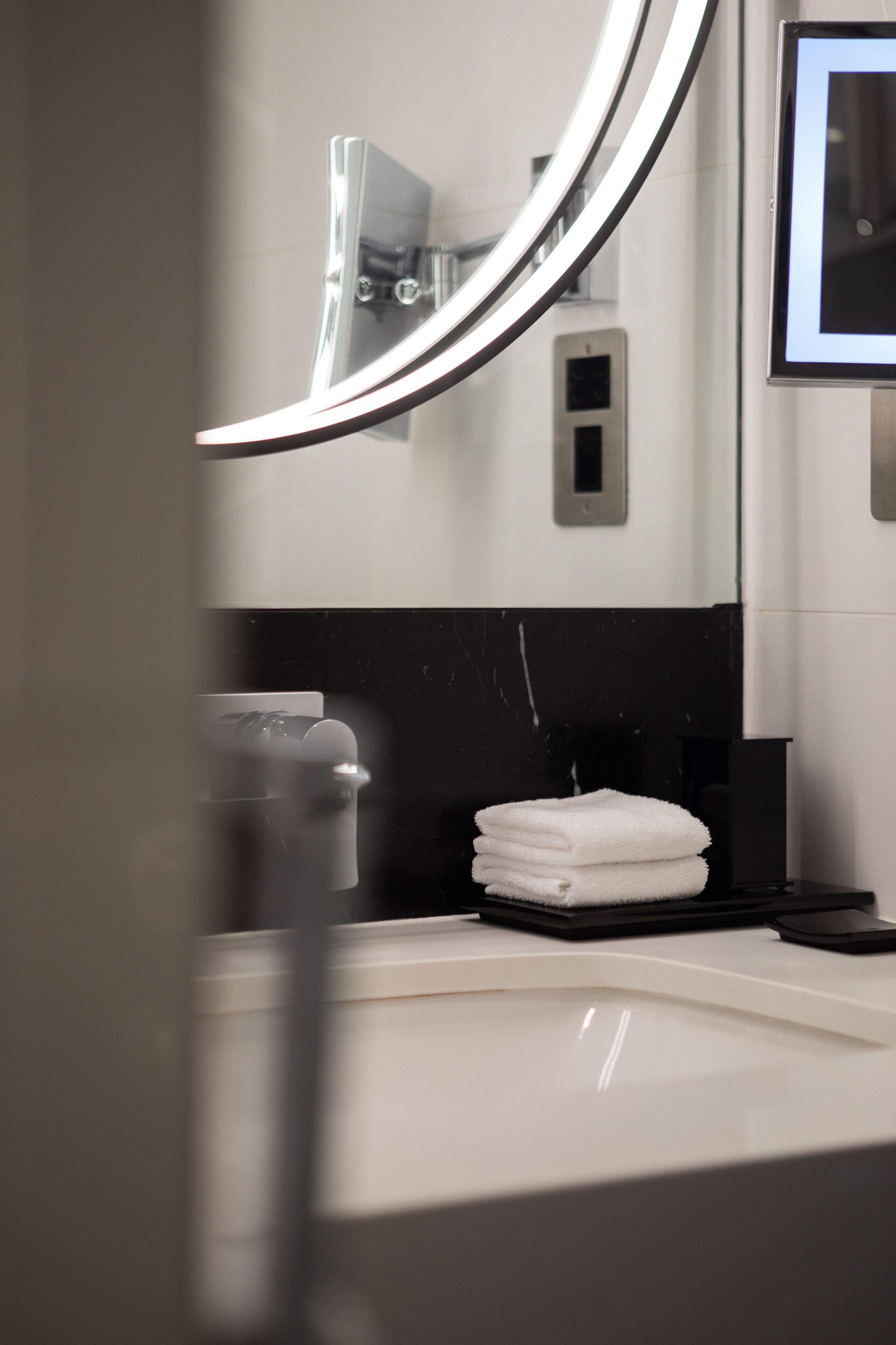 A bathroom with a white sink, a mirror, and a towel stack.