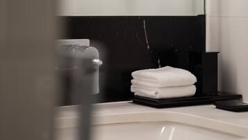A bathroom with a white sink, a mirror, and a towel stack.