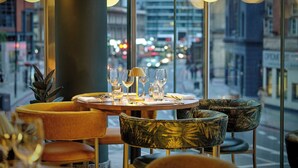 A restaurant with a table set for two, large windows, and city views. - Montcalm East, Autograph Collection (London)
