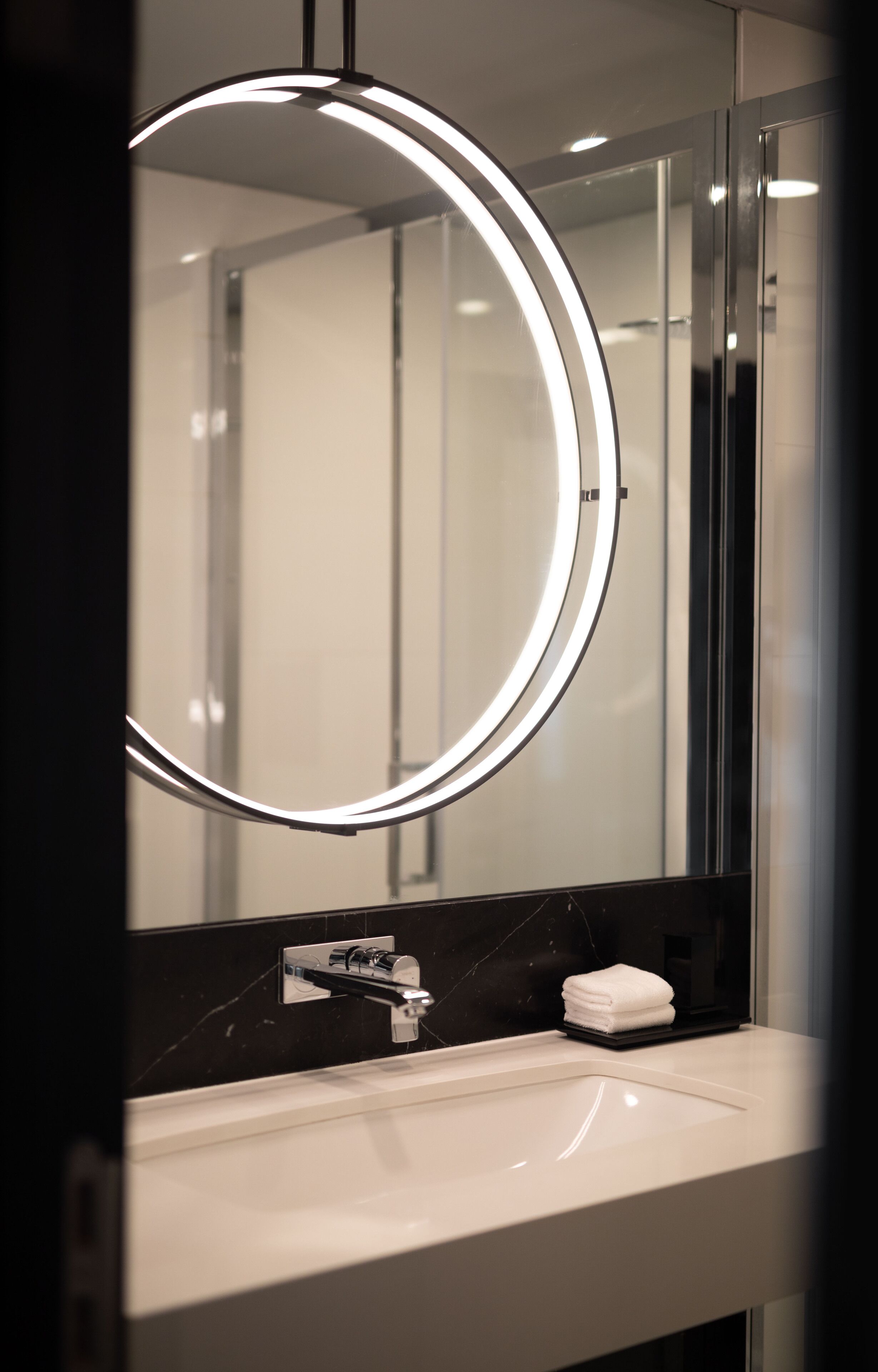 A modern bathroom with a circular mirror, a white sink, and a black marble backsplash.