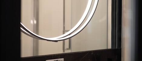 A modern bathroom with a circular mirror, a white sink, and a black marble backsplash.