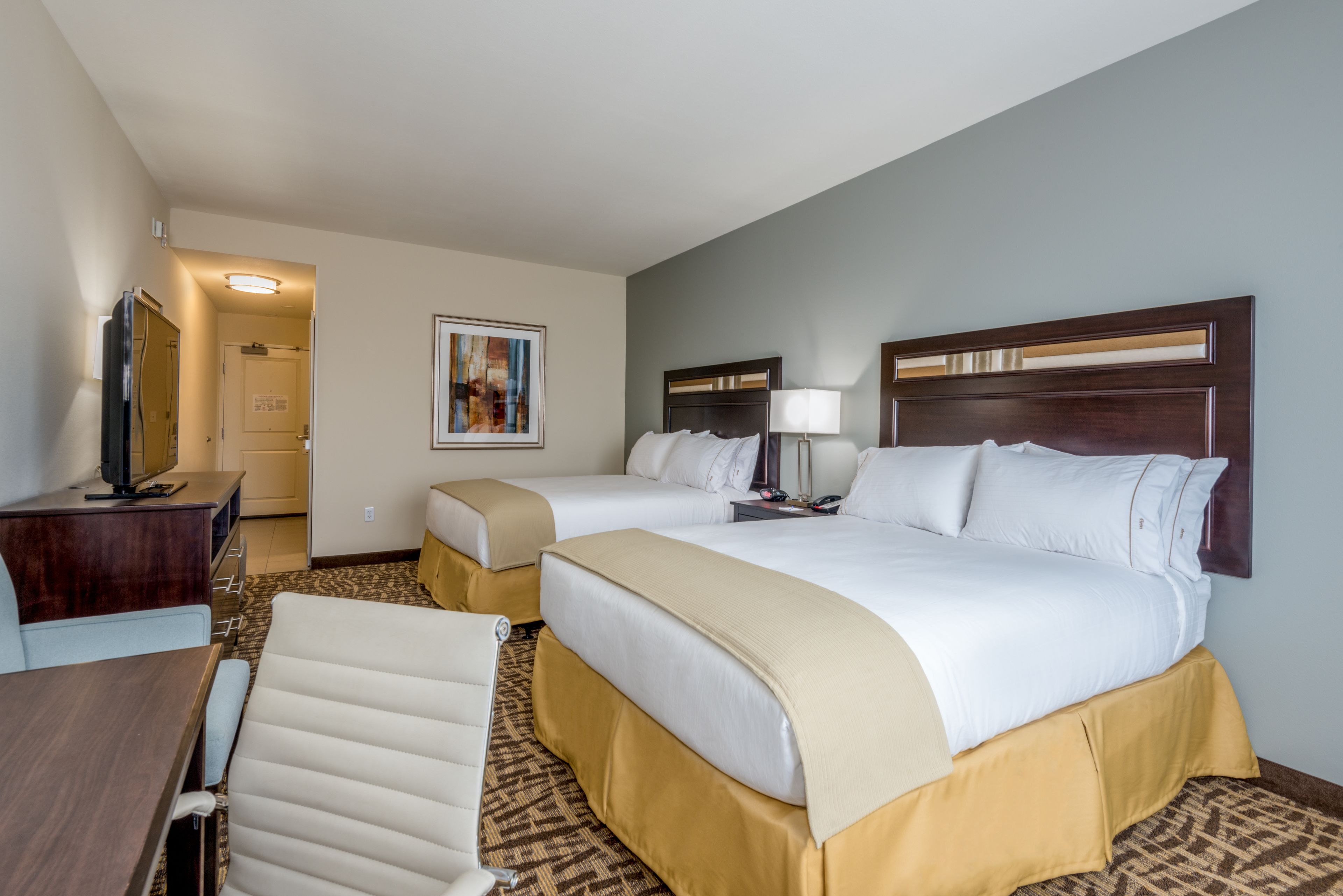 A hotel room with two beds, a desk, a chair, a TV, and a painting on the wall.